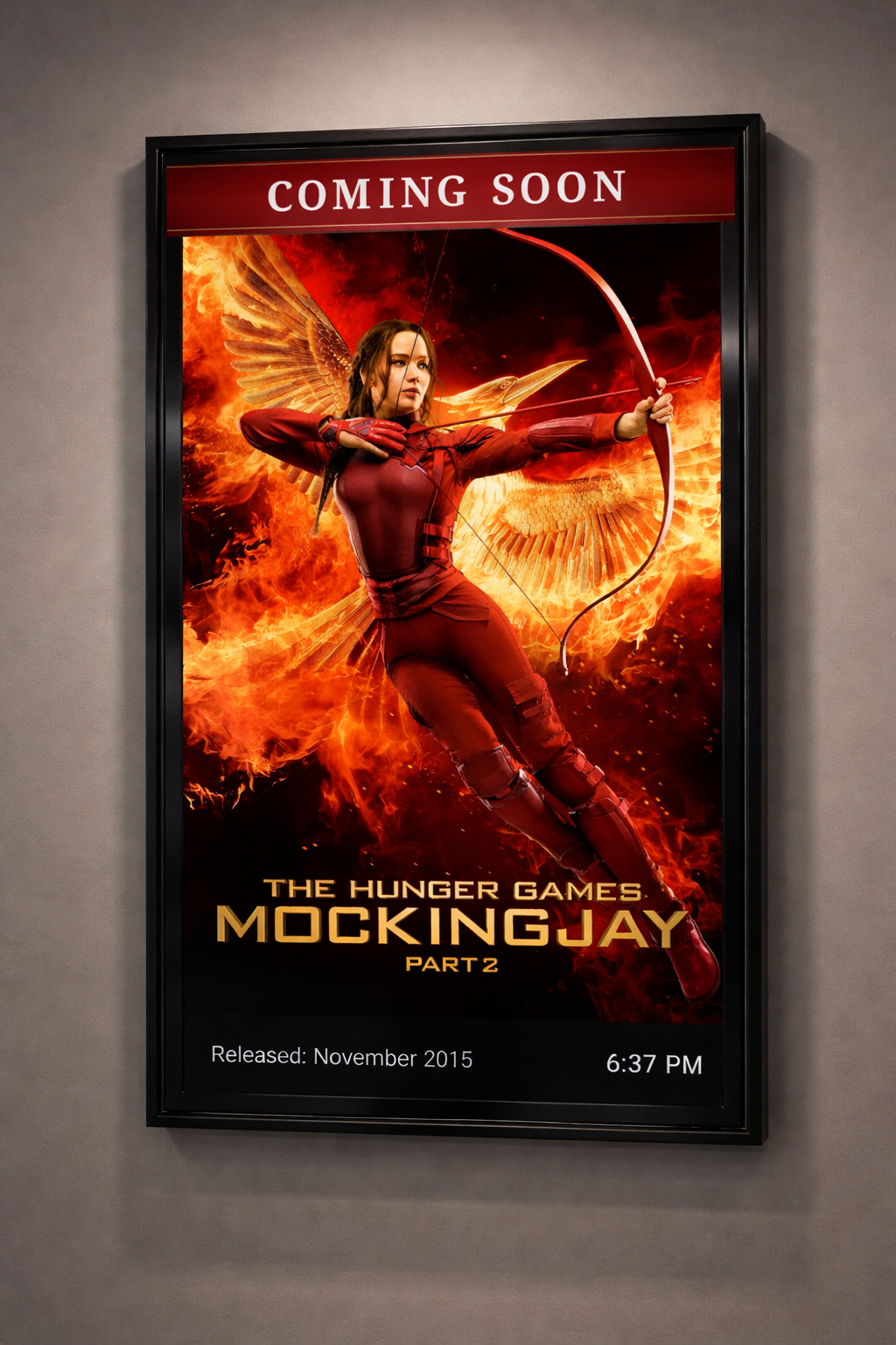 PosterBox displaying The Hunger Games: Mockingjay Part 2 movie poster on a portrait-mounted TV in a black frame, with Coming Soon header, release date, and real-time clock