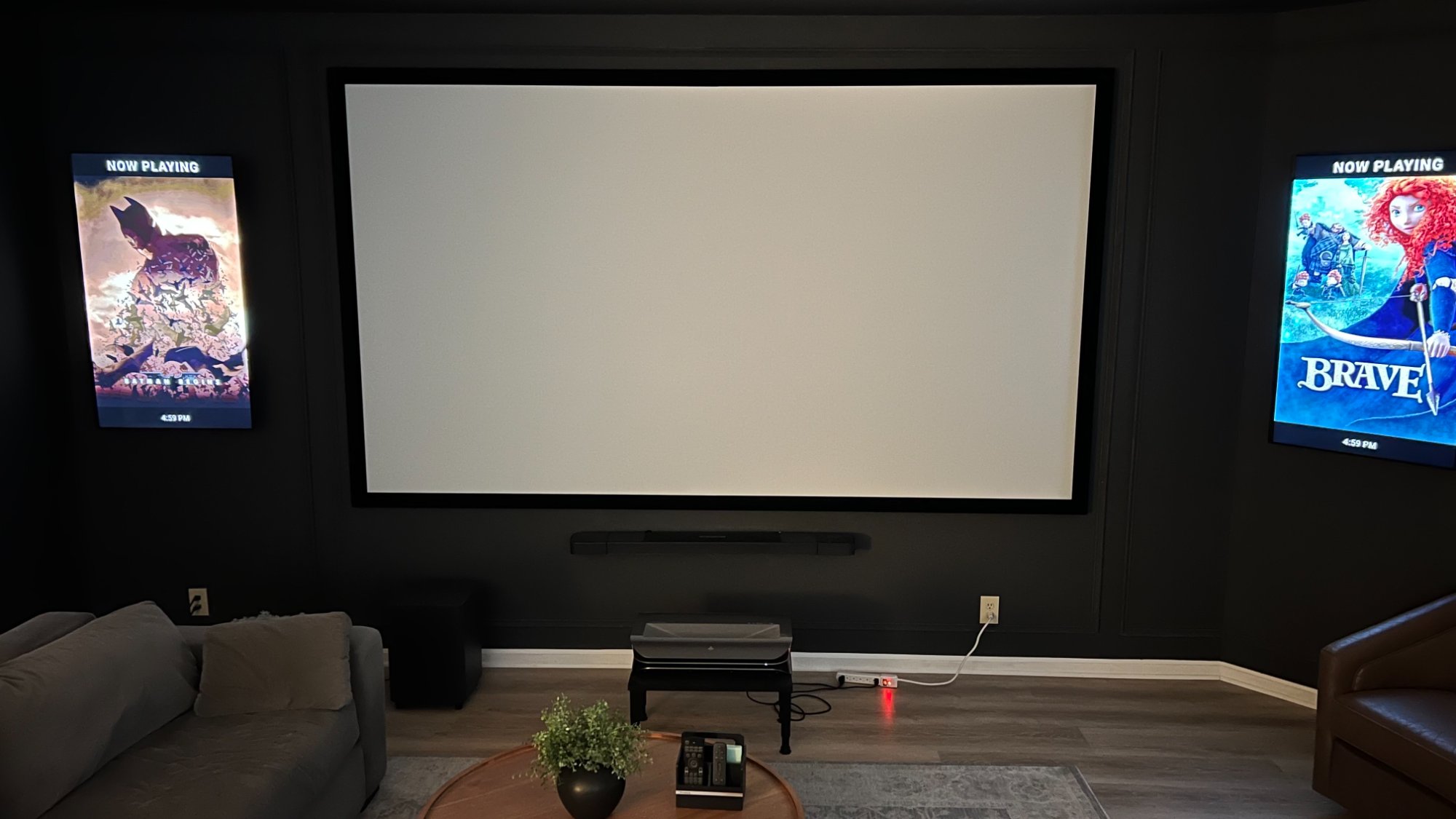 PosterBox running on two portrait TVs flanking a home theater projector screen, displaying movie posters for Batman and Brave